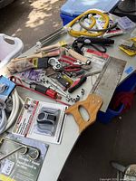 Photo showing a variety of hand tools arranged on a table including paint brushes, pliers, screwdrivers, and a wooden-handled hand saw.