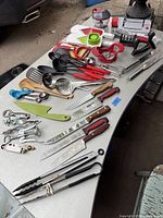 Overhead view of assortment of kitchen utensils and knives on table, showing variety and condition.