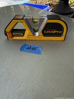 Yellow and black Laser Level Pro device with two bubble levels and laser label on front, placed on outdoor table.