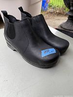 Pair of men's black leather Dansko boots size 42 with elastic side panels, low heel, and pull tabs on back, shown on white surface.