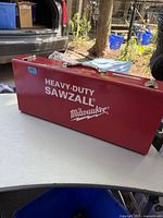 Closed red metal Milwaukee Sawzall carrying case showing front design and handle.