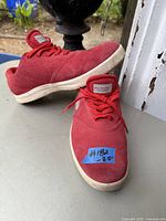 Pair of red suede Nike running shoes on table outdoors, showing side profile and overall condition
