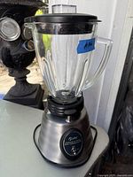 Photo showing an Oster Professional Series blender with a 6-cup glass jar, black lid with center cap, stainless steel base with toggle switch and branding.