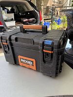 Closed black Ridgid toolbox on table with visible brown grip handle, orange accents and logo, and latches.