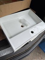 Photo of white rectangular porcelain sink with faucet hole and drain hole, new in box.