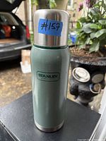 Thermos placed upright showing green textured body, stainless steel lid and base with Stanley logo on front.