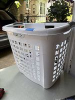 Photo showing a white Sterilite laundry hamper made of plastic with square ventilation holes, gray handles, and normal wear signs.