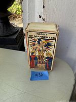Photo of the Tarot of Marseilles deck in original box standing upright, showing colorful illustrated box art with cherub and three figures.
