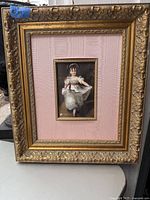 Full view of the gilded ornate wood frame with central portrait and pink mat.