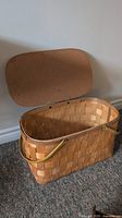 Large woven wicker picnic basket with hinged lid open, showing interior and brass side handles