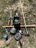 View of all assorted outdoor garden tools laid out on grass including Scotts turf builder spreader, shears, sprinklers, gel knee pads, measuring stick and weed cutters.
