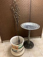 Photo showing birdbath, ceramic planter with sunflower design and solar floral tree all together against a brown woven screen