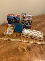 All items displayed on table: Puzzle Rollup box, Art Gallery 6 puzzle pack box, The Couples Quiz game, blue Bosc speaker, wooden travel backgammon/chess set.