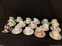 Front view of 16 vintage teacups and saucers arranged in two rows showing various floral and decorative patterns.
