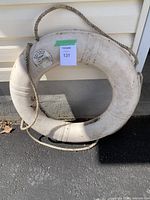 Front view of the used white Dolphin life buoy showing wear and an attached rope.