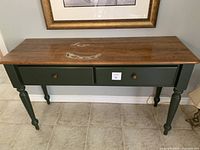 Front view of farmhouse console table showing wooden top with damaged areas and green base with drawers.