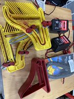 Three yellow Featherboard spacers with red adjustable knobs, two Motomaster 12V battery chargers, and a packaged blue Wrap-n-Strap cord strap, all on a wooden surface.