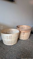 Photo showing two wooden bushel baskets placed on carpet with natural wooden slats and metal handles.
