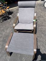 Full view of IKEA Poang lounge chair with matching stool showing dark wood frames and gray fabric cushions in outdoor lighting.