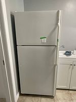 Full front view of white Maytag Plus refrigerator with freezer on top, showing door handles and adjacent cabinetry.