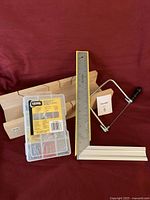 Wooden mitre box with angle slots, Lee Valley square ruler, plastic box of assorted screws and hardware, coping saw handle visible