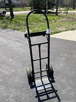 Full front view of black metal moving cart, showing overall structure with 2 large rear wheels and handle.
