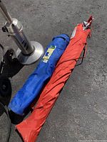 Blue and red bags for folding camp chairs next to propane heater base and hose cart on wheels.