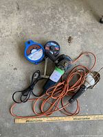 Mastercraft electric angle grinder with orange power cord alongside abrasive disks and plug-in light on concrete floor with reference ruler
