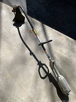 Full view of Ryobi electric string trimmer with telescopic pole laid on concrete floor showing the motor housing end and the cutting end with debris guard.