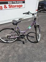Full side profile of the purple Schwinn woman’s bike in outdoor setting on asphalt. Shows overall condition, frame, tires, seat and handlebars.