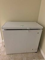 Front view of white GE chest freezer with lid slightly open showing latch and smooth exterior finish.
