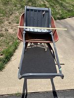 Black plastic snow shovel lying on the ground showing ribbed blade and metal handles.
