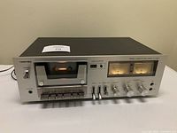 Front view of Toshiba stereo cassette deck with cassette compartment, control buttons, and VU meters.