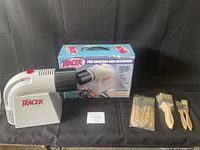 Artograph Tracer projector positioned beside its original box and grouped paintbrushes in various sizes, some still packaged.