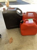 Two red jerry cans and one red oil drain container on a concrete floor outdoors, showing size and condition.