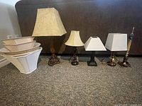 Wide view of all five table lamps lined up against the sofa with five varying lampshades stacked to the left.