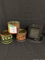 Side view showing three vintage chewing tobacco tins and a small black space heater, all items visible together