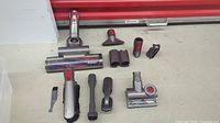 Wide shot showing all Dyson vacuum spare parts on a flat surface with a red background edge.