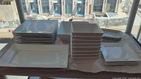 Stacked white rectangular and square plates along with bowls and platters.