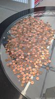 Glass table surface covered with a large number of scattered copper penny coins in various conditions.