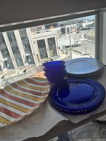 Wide shot of all items including cobalt blue glass bowls, charger plates, silver-toned charger plates, and ceramic multicolor striped platter.