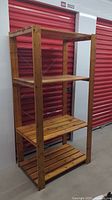 Wood shelving unit made of wood with natural finish, front angled view showing four shelves and vertical support with holes.