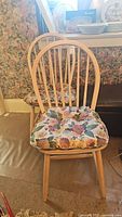Front view of one beachwood dining chair with floral seat cushion in a room with floral wallpaper.