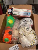 Top view of an open cardboard box showing colorful sports balls sealed in clear plastic and the boxed Auto Prix foot pump on top