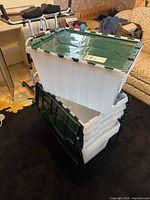 Stacked seven white plastic storage bins with attached dark green hinged lids, two different lid styles visible.