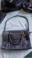Photo of large black leather handbag with double handles and tassel detail.