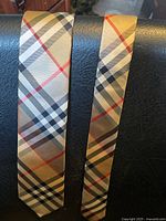 Close-up view of the tie showing the beige fabric with the classic Burberry check pattern consisting of black, white, and red lines.