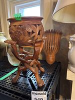 Carved wood pot on stand beside a wood sconce on a shelf near a lamp