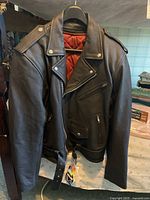 Front view of black leather motorcycle jacket showing angled zipper pocket and waist belt.