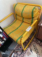 Front angle view of the yellow tubular metal frame chair showing chipped paint and fabric upholstery with green stripes.